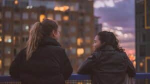 two women standing near railing looking thoughtfully at each other