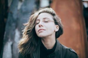 closeup of woman wearing black closing her eyes and breathing deeply to help her manage stress in recovery